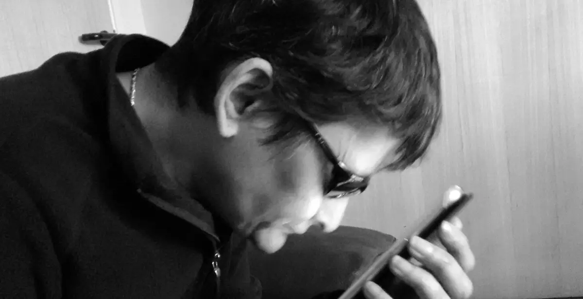 User with sunglasses looking at phone. Greyscale photo.