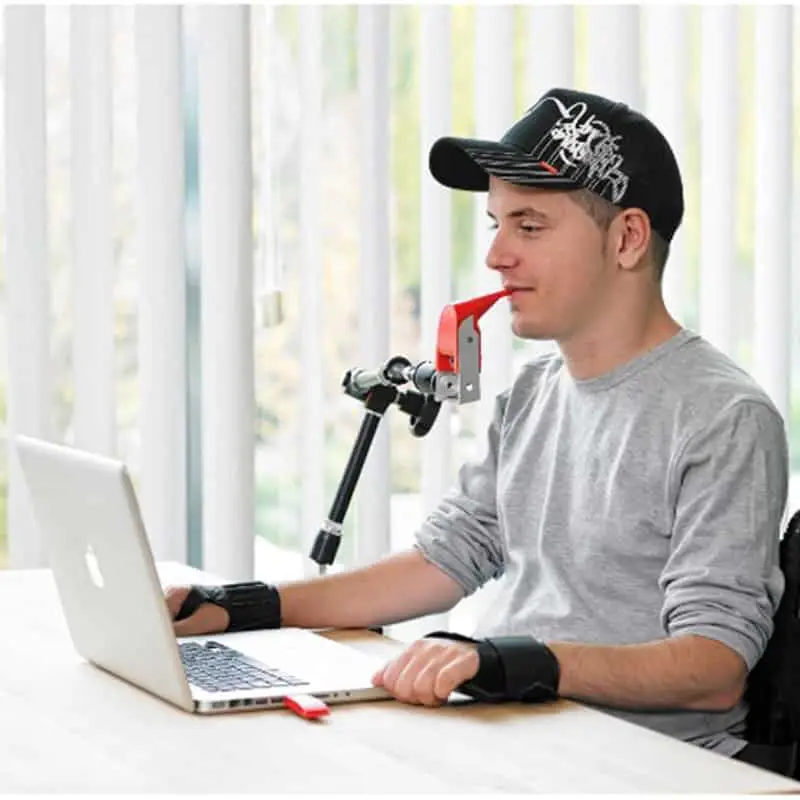 Young man by his laptop with red device in mouse that looks kind of like an astma inhaler.