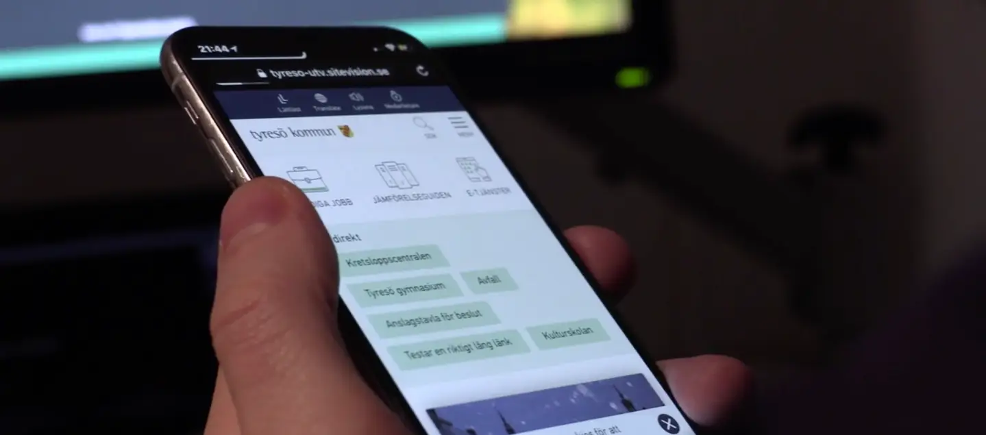 Närbild på hand som håller i mobil med Tyresö kommuns webbplats på skärmen.