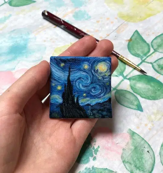 Tiny painting of castle in night sky held in the palm of a hand. 