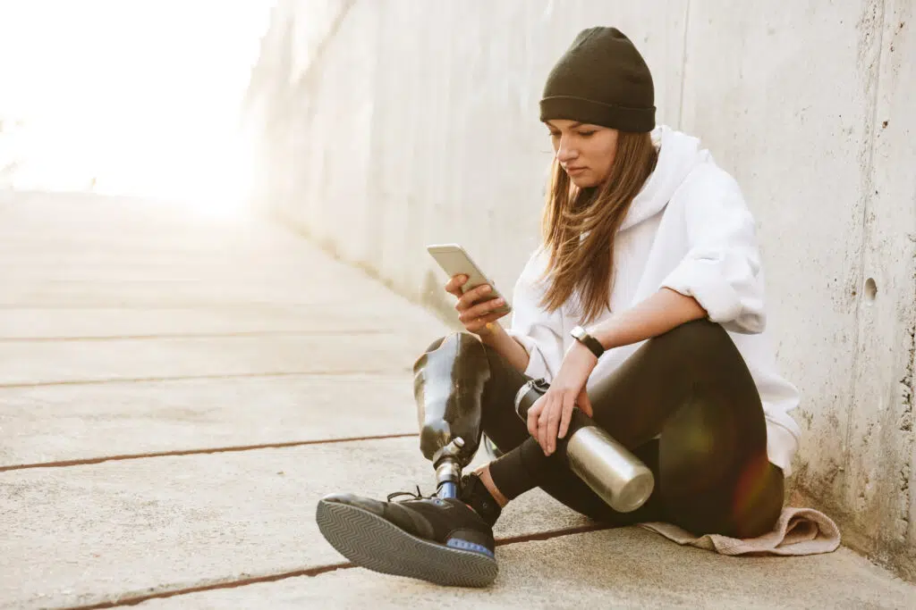 Woman with prosthetic leg sitting cross-legged and using smartphone.