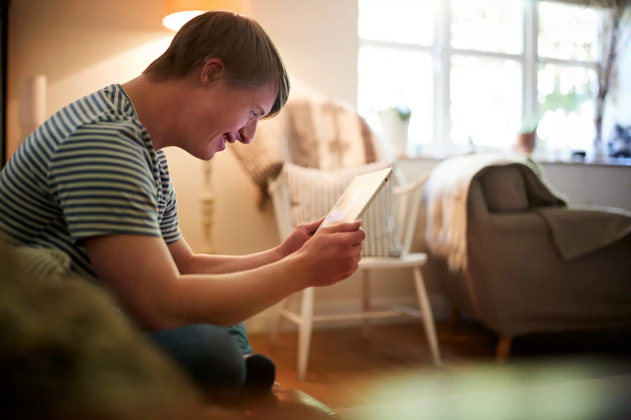 Person with Down Syndrome looking at an iPad in his sofa.