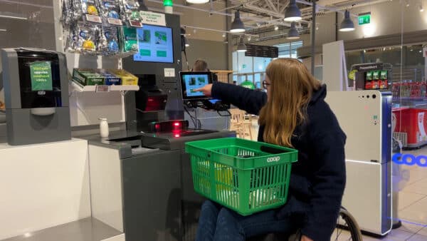 Person in wheelchair using a lower screen by a self checkout machine in a grocery store.