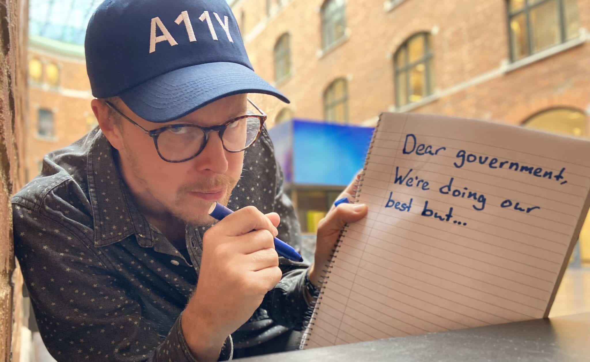 Hampus in a11y cap with note pad saying "Dear government we're doing our best but..."