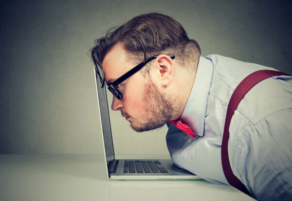A man with glasses resting his forehead against the laptop screen.