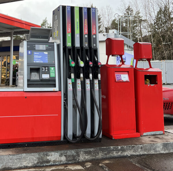 Gas station fuel pumps, payment terminal and trash cans placed on a raised ledge.