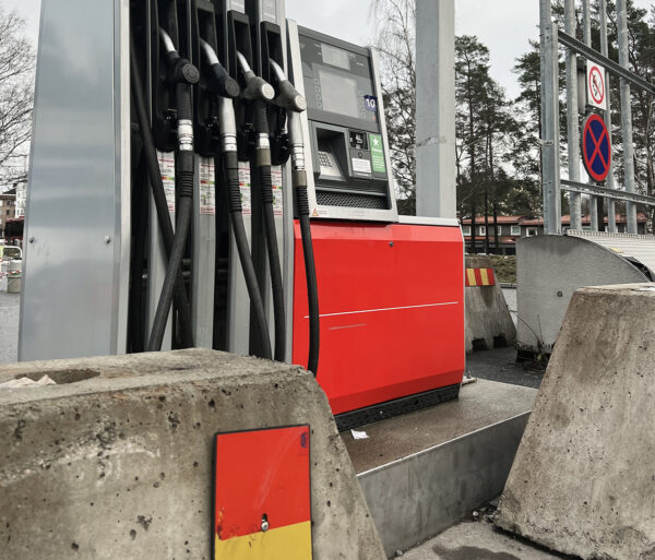 Gas station fuel pumps and payment terminal on a high ledge. Large concrete barriers in front of the ledge partly block access to the controls.