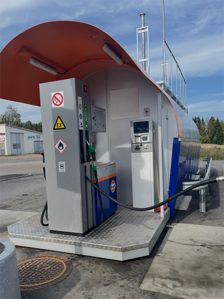 Gas station pump on a raised, narrow platform with a payment terminal mounted high and facing away from ground level.