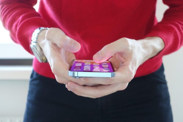 A person holding an iPhone in both hands, with the screen unlocked and app icons visible.