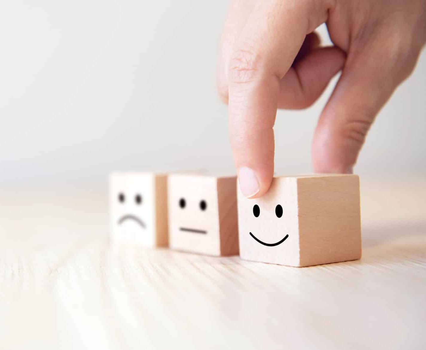 Wooden blocks with sad and happy smiley faces placed on table.